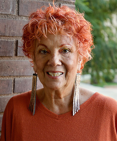 woman with orange shirt and long earrings smiling at the camera